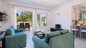 Un salon moderne avec des canapés de couleur turquoise, une table basse et un téléviseur. Il y a un balcon avec une piscine et du mobilier d’extérieur.