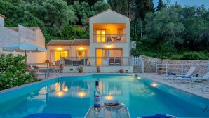 Un bâtiment à deux étages doté d’une piscine, de chaises longues et d’une table sur laquelle se trouvent une bouteille et un saladier.
