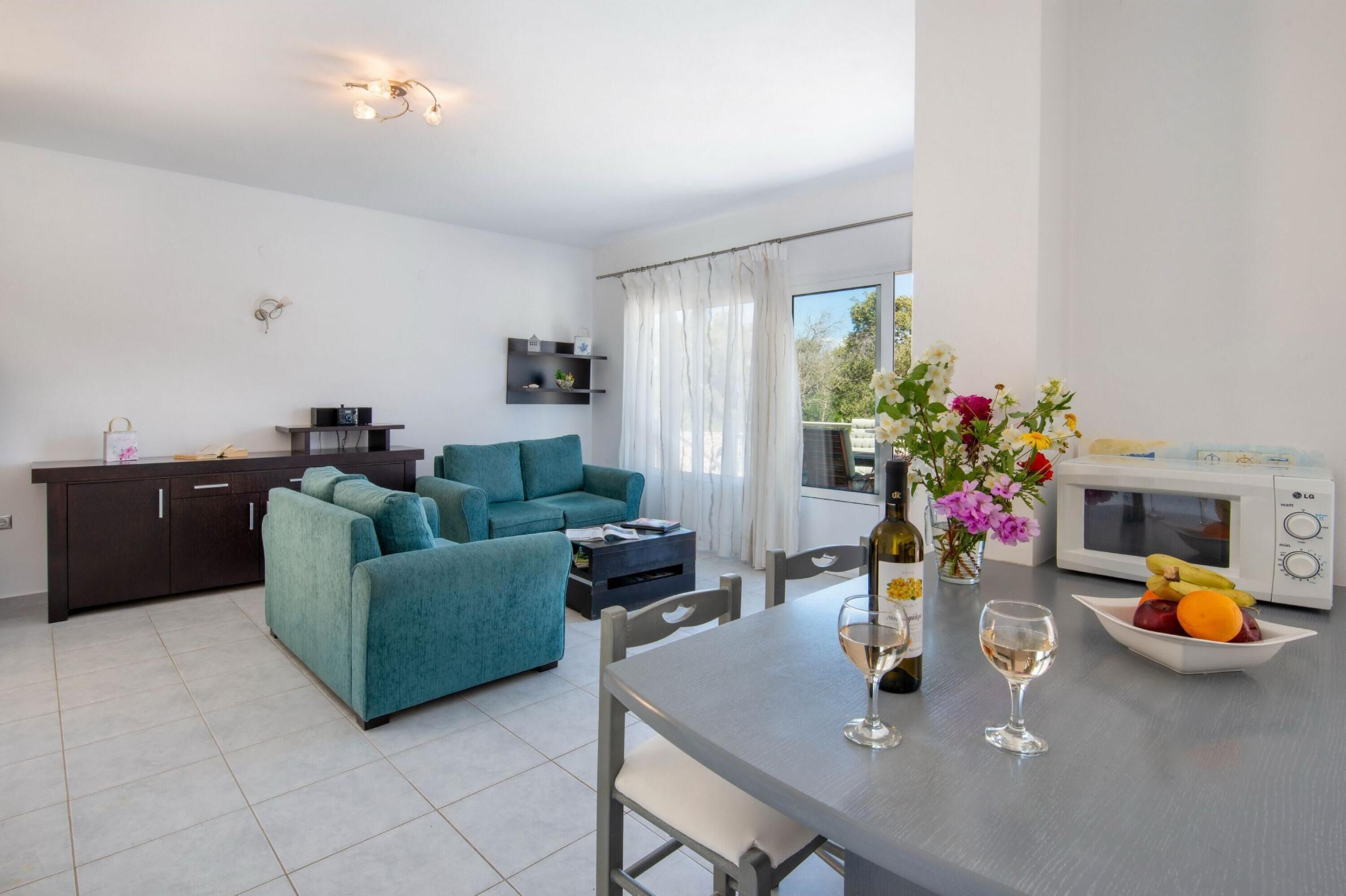 Una sala moderna con un sofá color turquesa, una mesa de comedor con una copa de vino y un frutero, un microondas y una encimera de cocina.