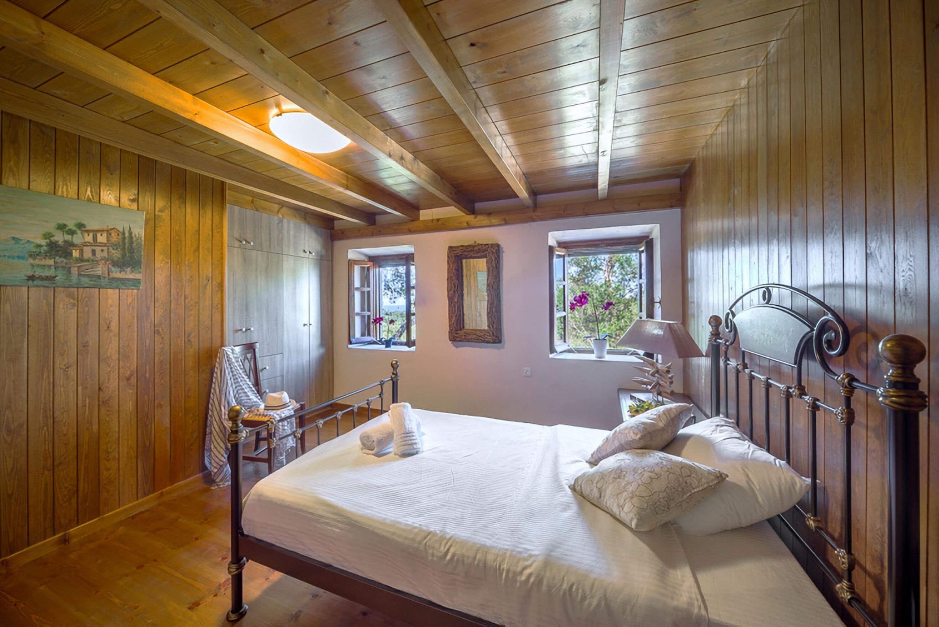 Un dormitorio con paneles de madera, una cama, ventanas y un cuadro en la pared.