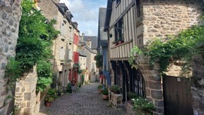 Una estrecha calle adoquinada flanqueada por edificios de piedra con entramado de madera y contraventanas rojas.