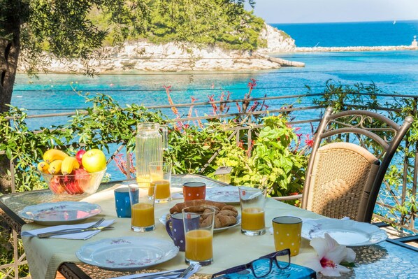 Une table dressée avec des aliments pour le petit-déjeuner, un verre de jus d’orange et une vue sur la mer et les falaises.
