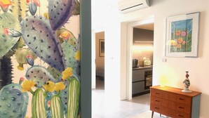 A hallway with a cactus painting, a wooden dresser, and a kitchen area with a framed picture on the wall. - Casa Lumi a in Syracuse (Syracuse)
