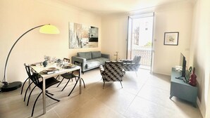A modern living room with a dining area, a grey sofa, a patterned armchair, and a large abstract painting on the wall. - Casa Lumi a in Syracuse (Syracuse)
