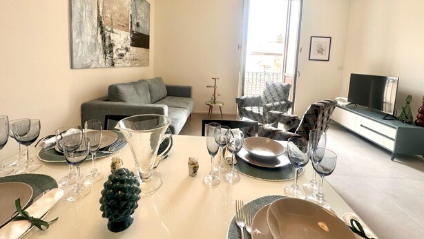 A dining area with a table set for a meal, a sofa, a chair, and a television in the background. - Casa Lumi a in Syracuse (Syracuse)