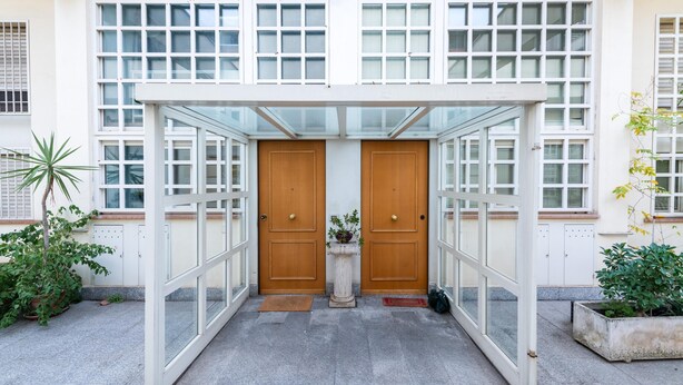 A covered entrance with a glass canopy, two wooden doors, and a potted plant in the center. - Loft Porta Maggiore in Rome (Rome)