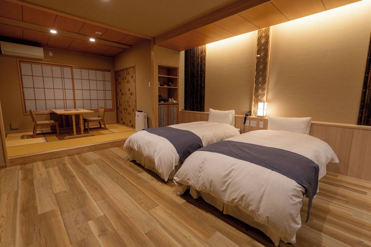 A hotel room with two beds, a sitting area with a table and chairs, and a wardrobe.