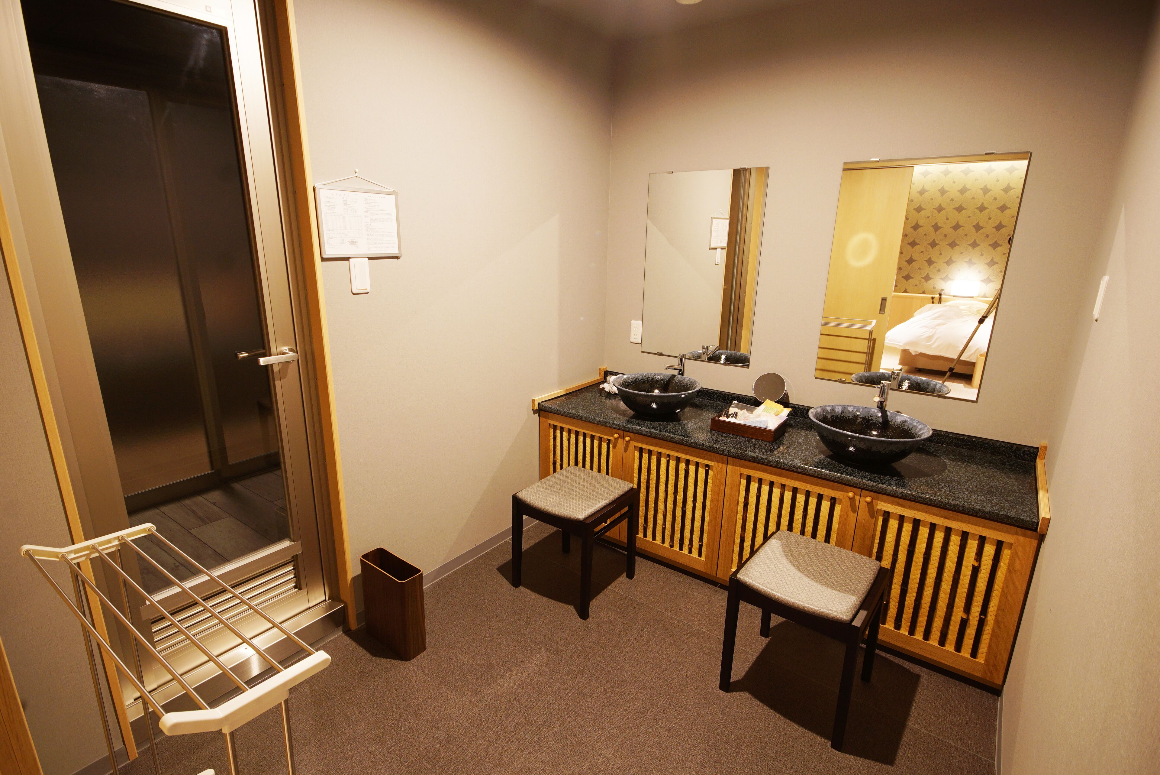 A compact bathroom with a sink, mirror, and two stools.