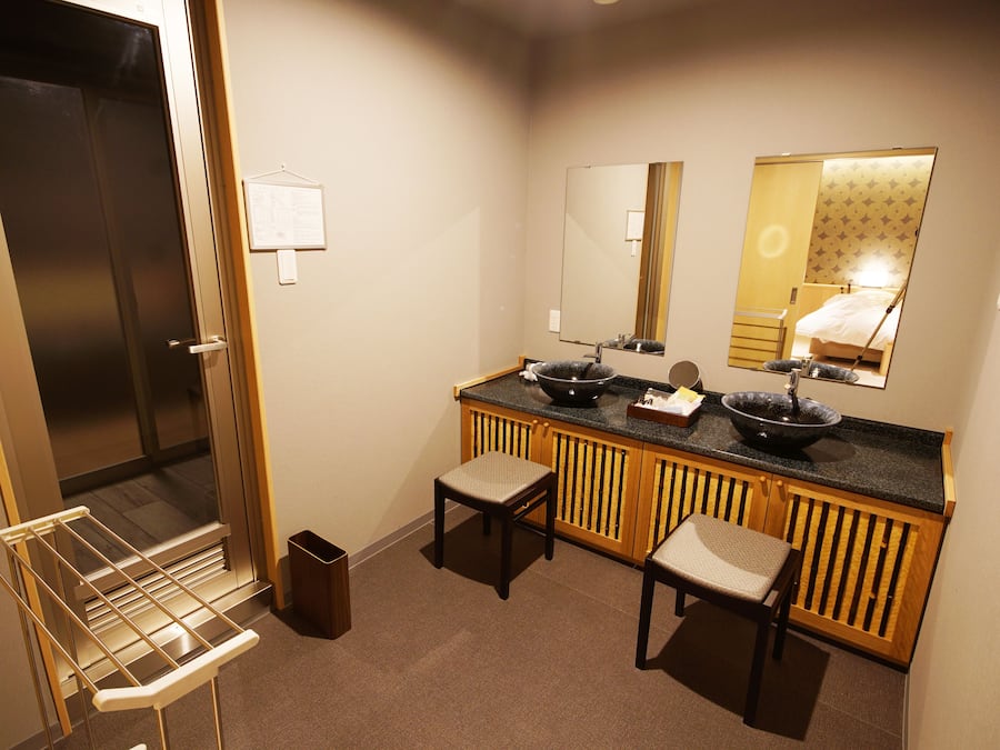 A compact bathroom with a sink, mirror, and two stools.