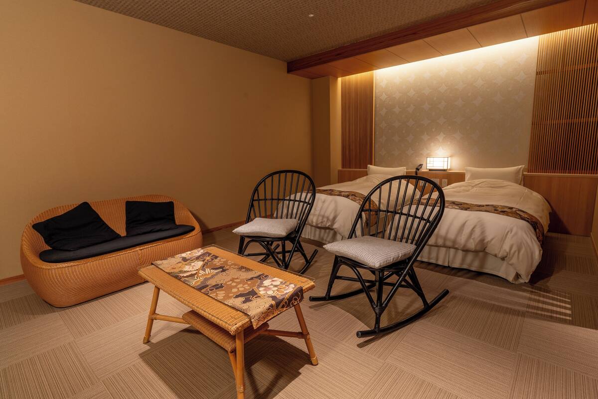 A hotel room with a sofa, two rocking chairs, a small table, and a bed with a nightstand and lamp.