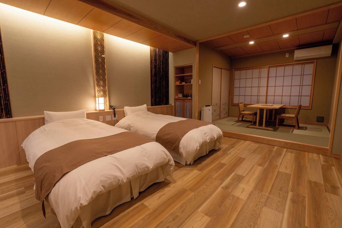 A hotel room with two beds, wooden flooring, a dining table, and a traditional sliding door.