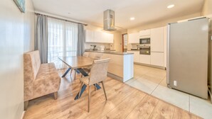 A modern kitchen with a central island, a dining area with a sofa and chairs, and a large refrigerator. - Kikambala Modern Apartment with Balcony (Nairobi)