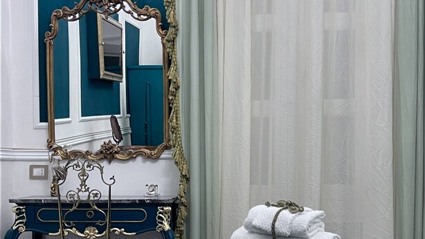 A hotel room with a bed, a vanity with a mirror, a desk, and a chair. There are towels on the bed. - Property Palazzo Caldarulo (Polignano a Mare)