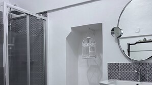 A bathroom with a glass shower enclosure, a sink with a mirror, and a birdcage decoration. - Property Palazzo Caldarulo (Polignano a Mare)
