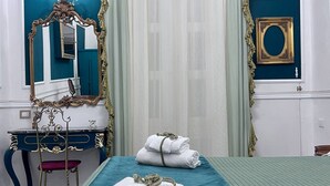 A hotel room with a bed, a vanity with a mirror, a dresser, and a window with curtains. - Property Palazzo Caldarulo (Polignano a Mare)