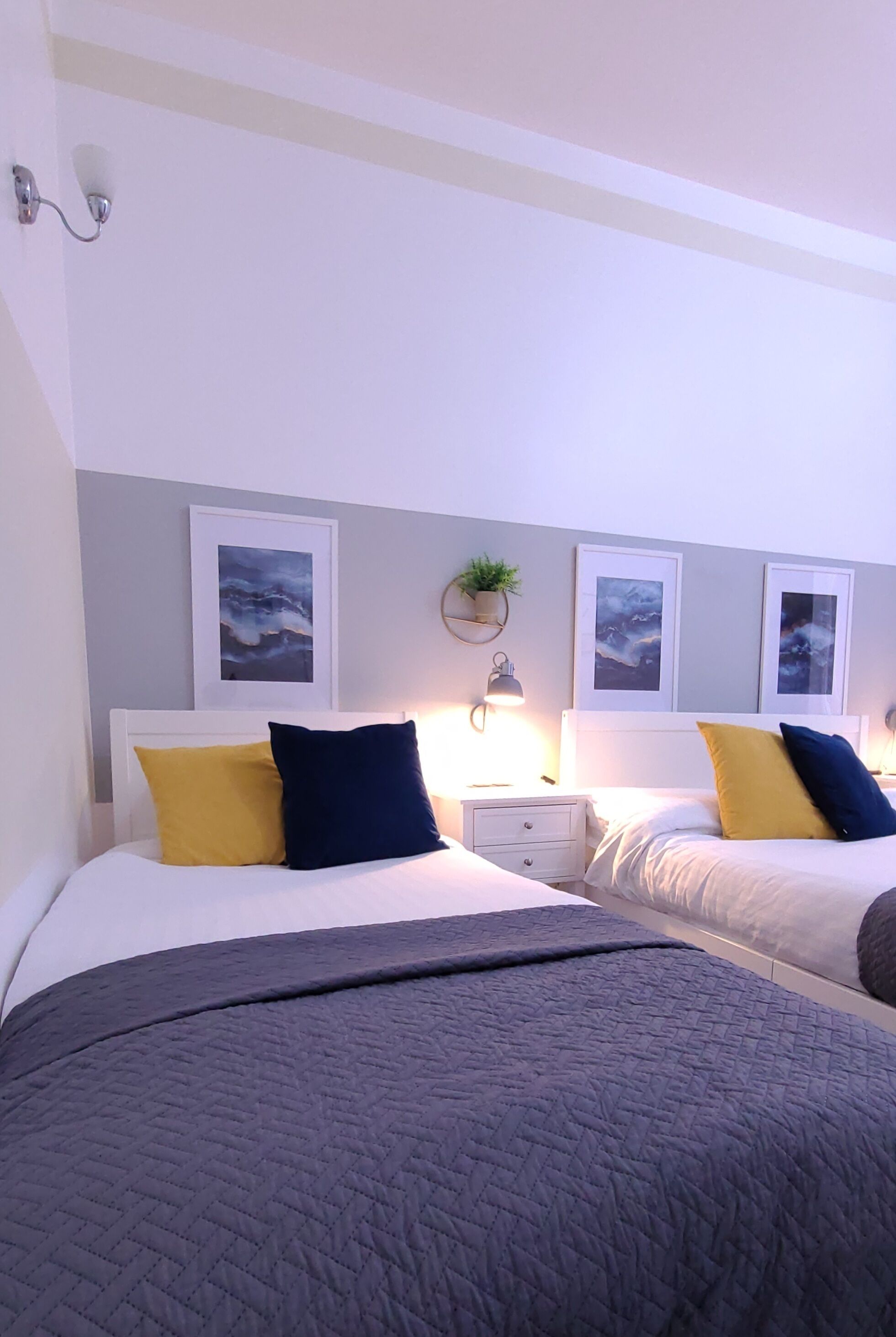 Una habitación de hotel con dos camas, una mesita de noche con lámpara y cuadros en la pared.