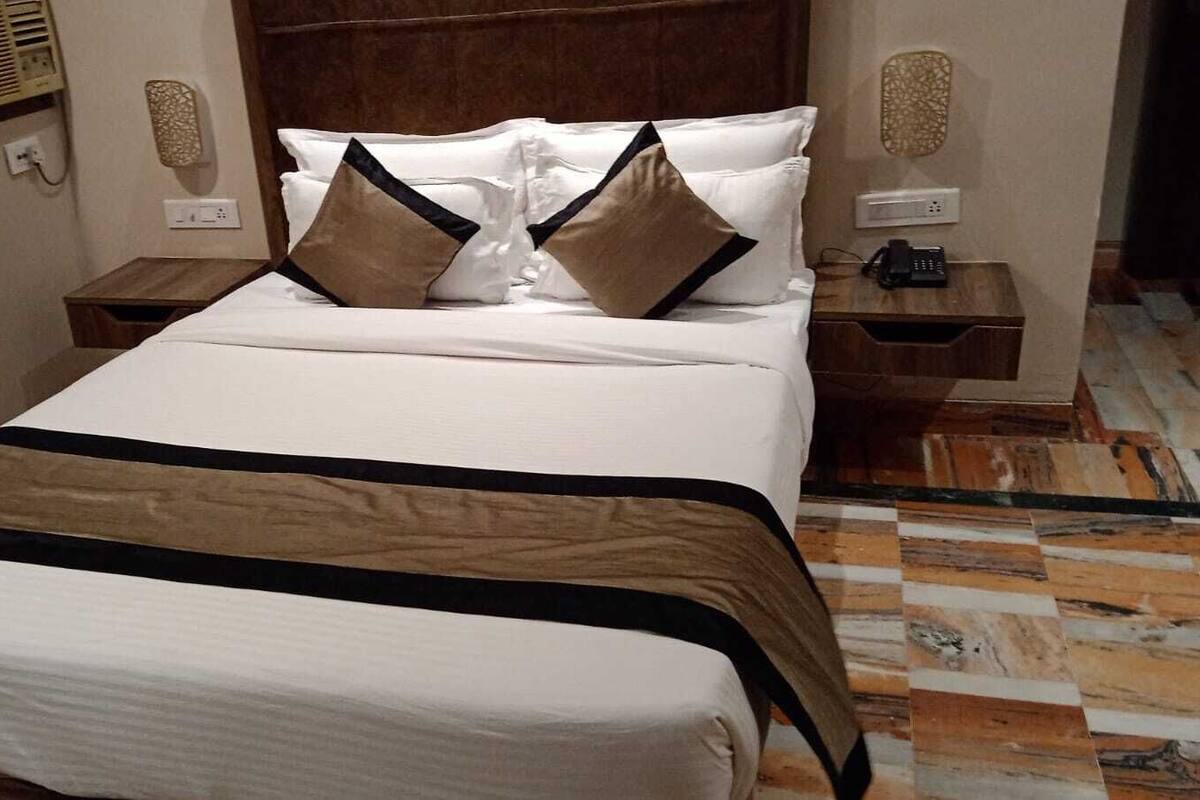 A neatly made bed with a white and brown bedspread, two bedside tables with lamps, and a patterned floor.