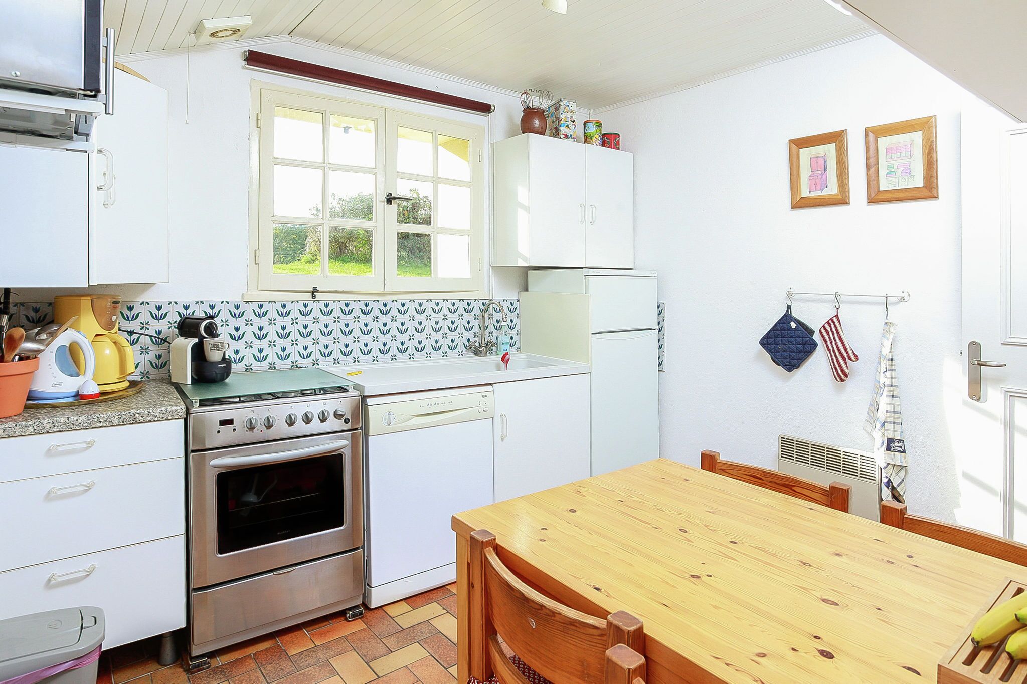 A kitchen with white cabinets, a stove, a dishwasher, a window, and a dining table.