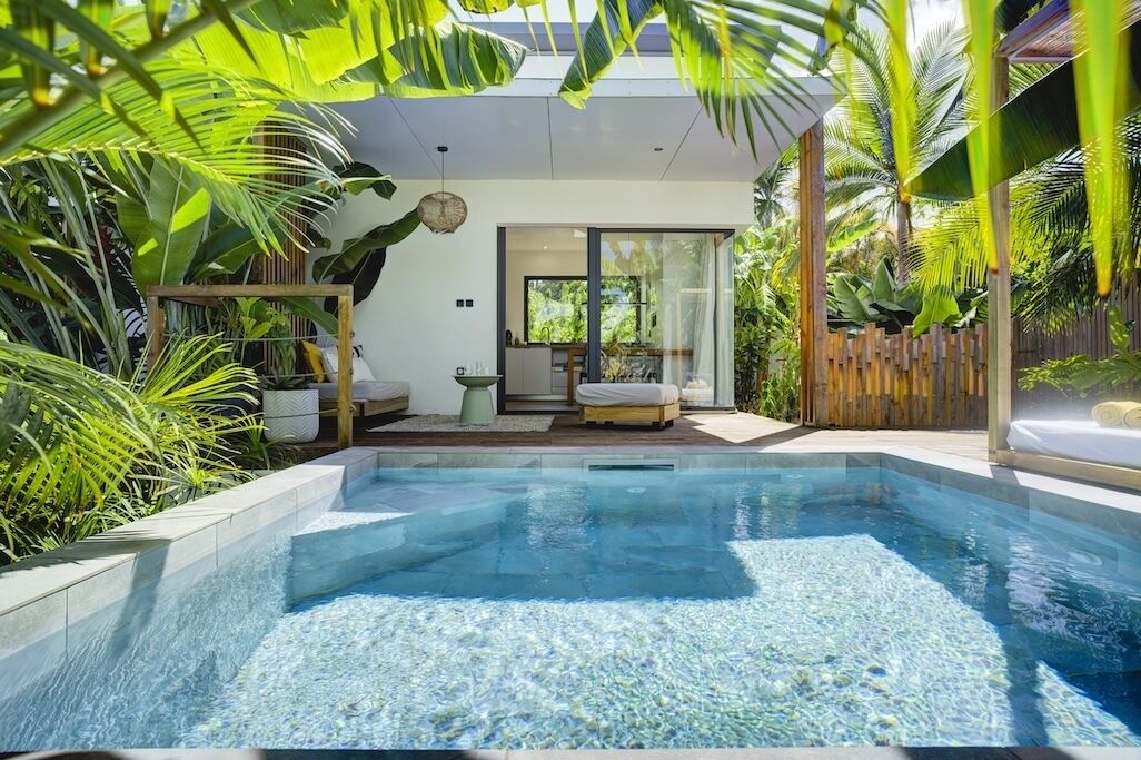 A modern pool area with clear water, surrounded by lush greenery and a wooden fence.
