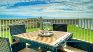 Un espacio de comedor al aire libre con mobiliario de mimbre y una mesa de madera, con vistas a un área verde y una cerca.
