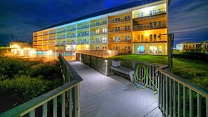 Un hotel de varios pisos con una zona de piscina y un paseo bien iluminado.