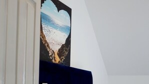 Ett sovrum med en säng, vita sängkläder, en mörkblå sänggavel och en tavla som föreställer en strandvy, upphängd på väggen.