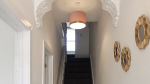 En smal hall med en trappa som leder upp till en våning ovanför. Väggarna är enkla, med ett element och dekorativ väggkonst.