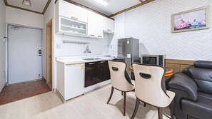 A compact kitchen with a refrigerator, microwave, and a sink. There are two chairs and a black sofa. - Geoje Youngsu Pension (Geoje)