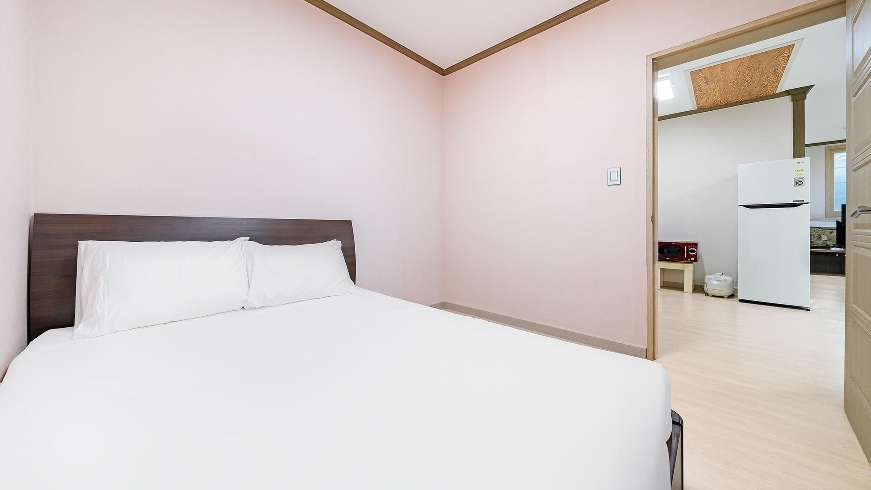 Habitación de hotel con cama, cabecera de madera, pared blanca y puerta que conduce a una zona de cocina.