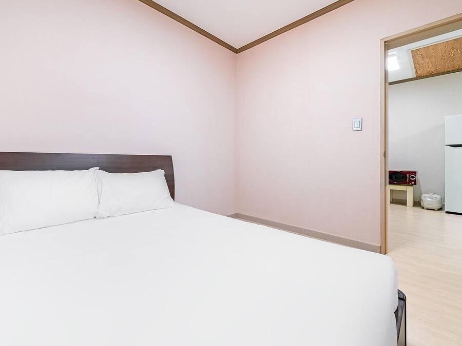Habitación de hotel con cama, cabecera de madera, pared blanca y puerta que conduce a una zona de cocina.