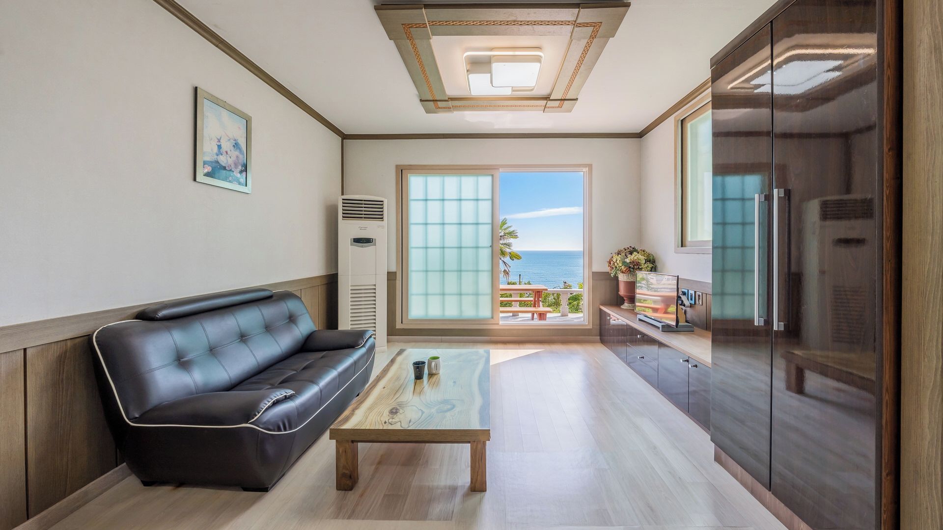 A modern living room with a leather sofa, a wooden coffee table, and a view of the sea through large windows.