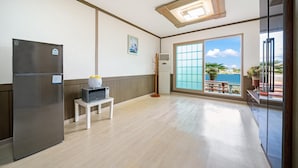 Une cuisine compacte équipée d’un réfrigérateur, d’un four à micro-ondes et d’une petite table. Une fenêtre donne sur un balcon agrémenté d’une balustrade et d’une plante.