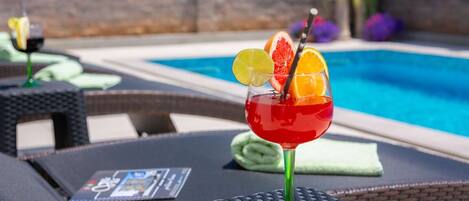 A poolside setting with lounge chairs and a cocktail glass with fruit garnish.