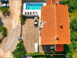 An aerial view of a property with a swimming pool, a covered carport, and a red-roofed building.