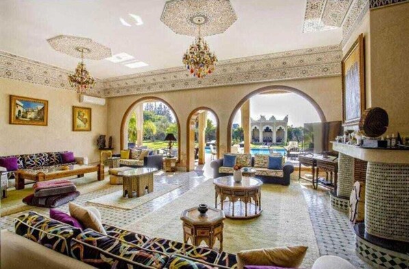 A spacious living area with a pool view, ornate ceiling, and traditional furnishings.