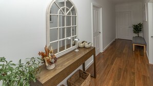 Un pasillo con una consola de madera, un espejo arqueado grande y una planta en maceta.