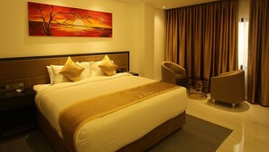 Una habitación de hotel con una cama grande, cabecera, mesita de noche, una silla y un cuadro en la pared.