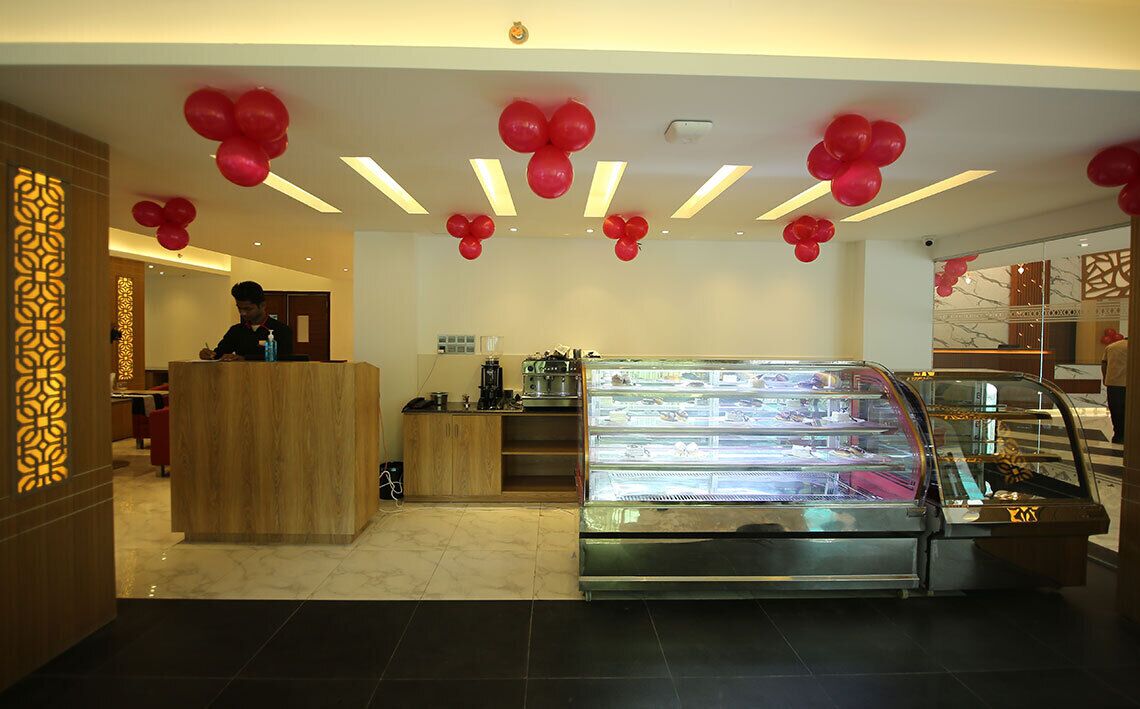 Hotellin vastaanottotiski, jossa on puinen palvelutiski, lasinen esittelyvitriini ja punaisia ilmapalloja.