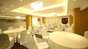 Un salón de conferencias con mesas redondas y sillas blancas, equipado con luces de techo y una lámpara de araña.