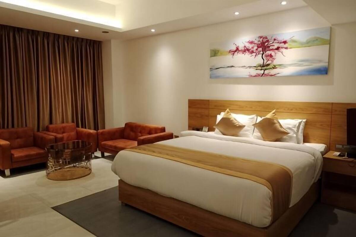 A modern hotel room with a large bed, two sofas, a coffee table, and a painting on the wall.