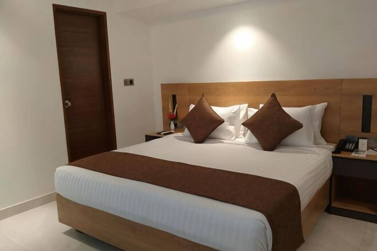 A hotel room with a large bed, wooden headboard, bedside tables, and a door.