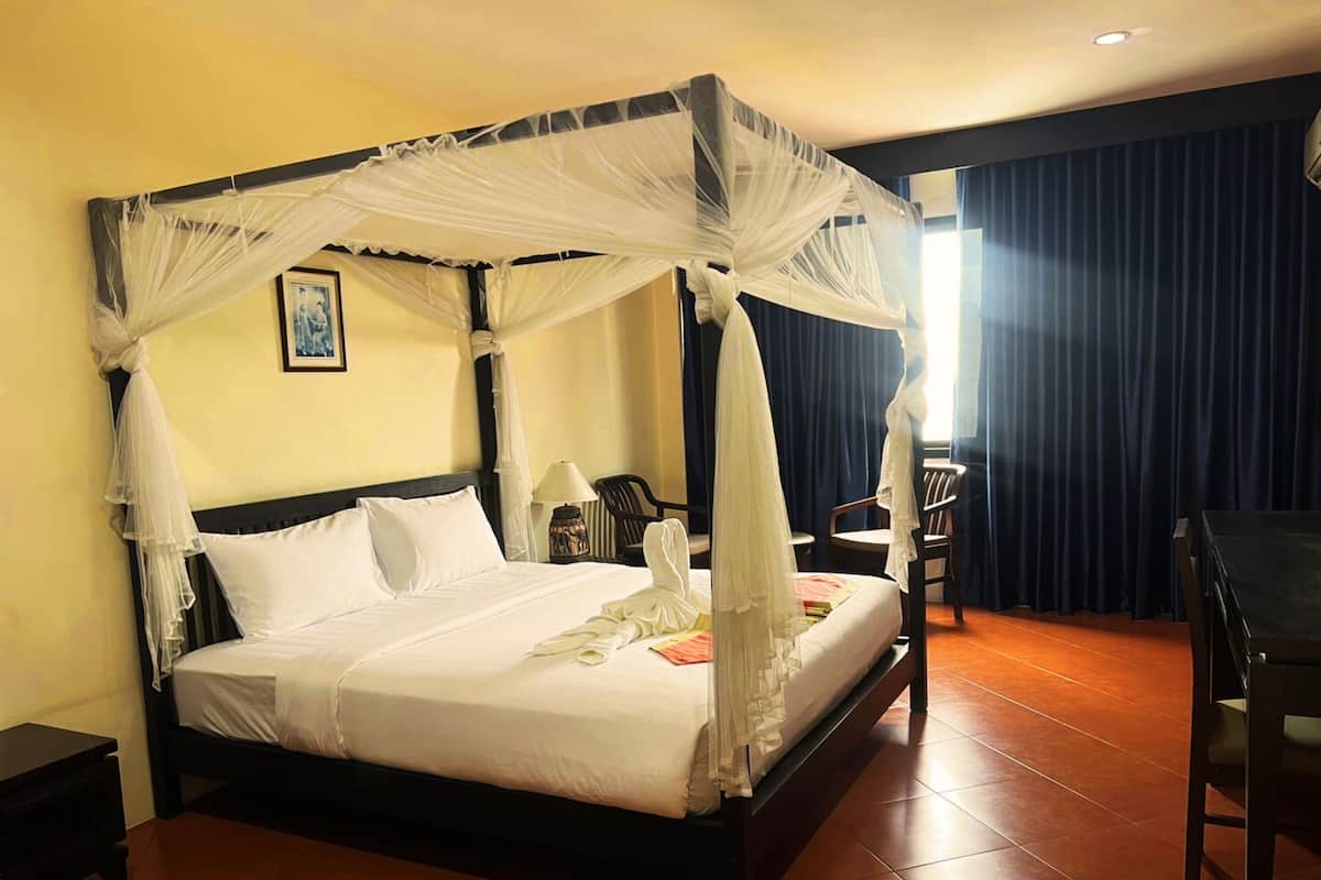 A four-poster bed with a canopy, a bedside table, a chair, and a desk with a chair.