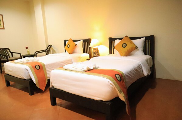 Two single beds with wooden frames, white linens, and orange decorative pillows.