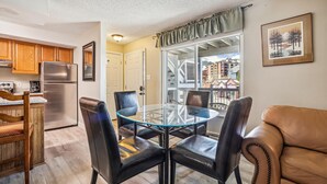 A dining area with a glass table and leather chairs, a kitchen with wooden cabinets, and a view of buildings through a window with curtains. - Dog-Friendly for Summer|Updated|On S. Main Street (Breckenridge)