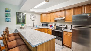A modern kitchen with wooden cabinets, a stainless steel refrigerator, a microwave, and a stove. There is a large window above the sink, and artwork on the walls. - Dog-Friendly for Summer|Updated|On S. Main Street (Breckenridge)