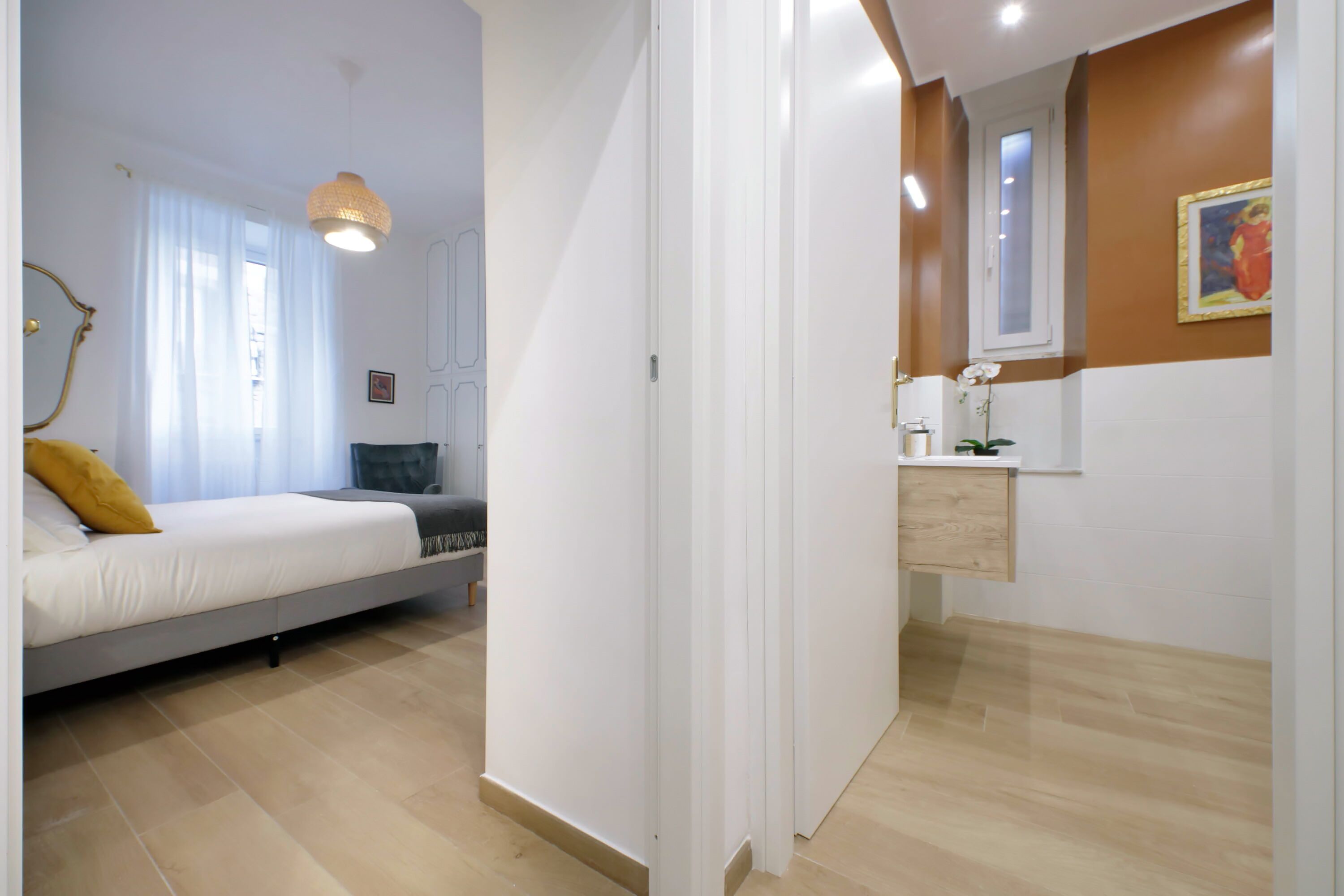 Un dormitorio con cama, mesita de noche, espejo y ventana con cortinas.