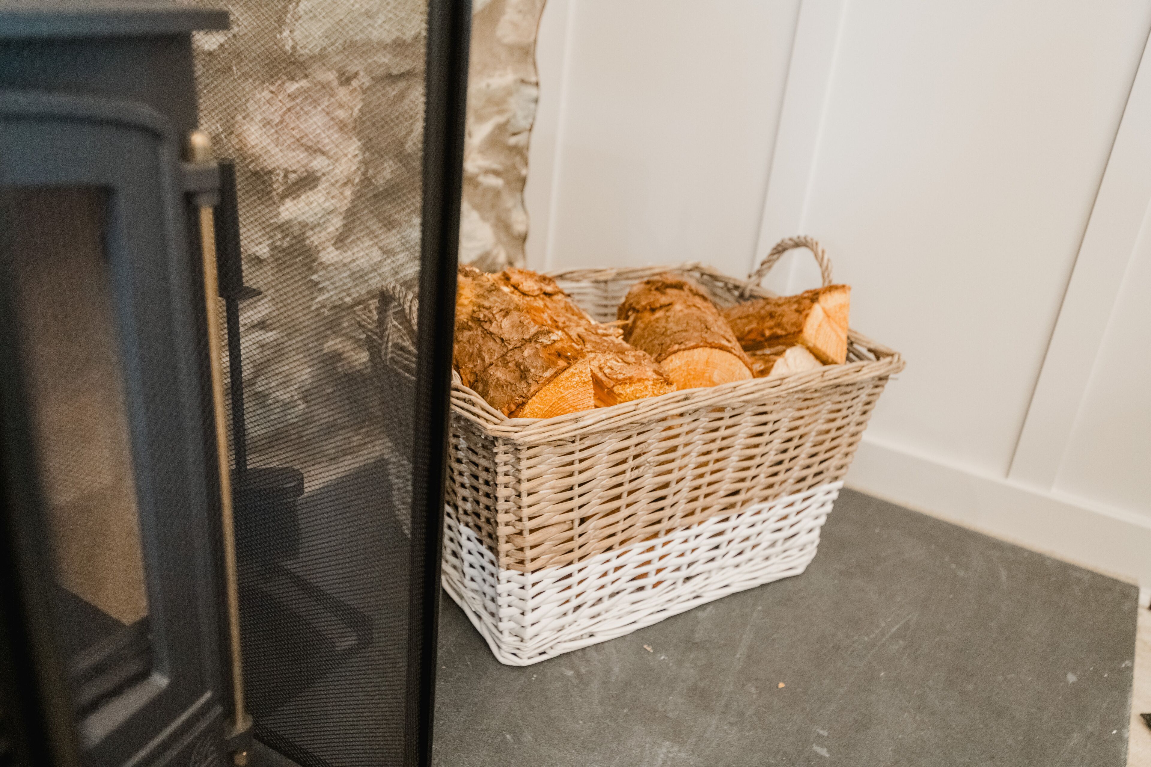 A wicker basket filled with bread placed on a dark surface next to a fireplace.