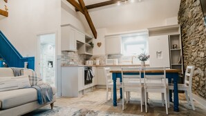 A cozy kitchen with white cabinets, a stone wall, and a blue dining area. - The Cow Shed at Pencraig (Holyhead)
