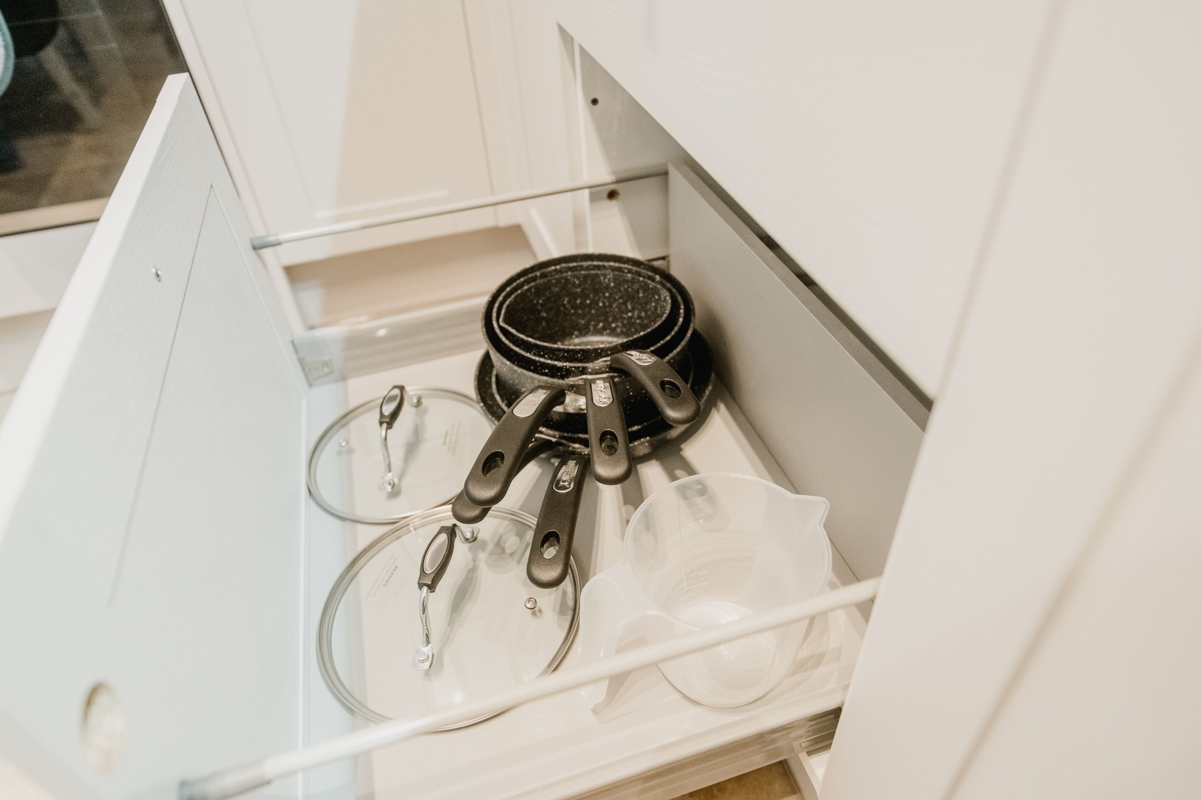 A kitchen drawer containing a frying pan, a glass measuring cup, and a plastic container.