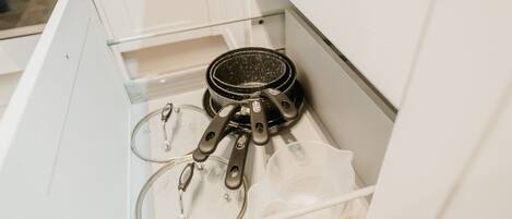 A kitchen drawer containing a frying pan, a glass measuring cup, and a plastic container.